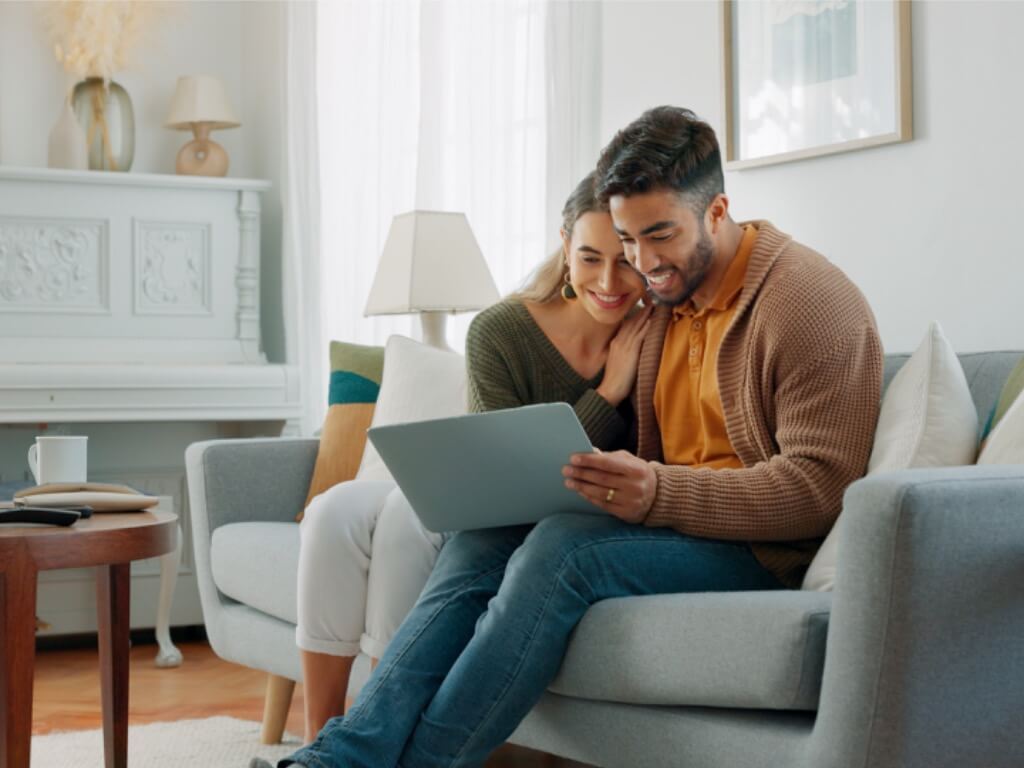 Laptop, living room and couple search website information for home investment, loan or real estate property discussion on sofa. Young people on couch with pc internet, planning future together
